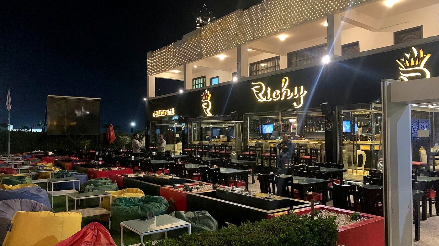 مبنى ريتشي لاونج ليلًا، ولافتتا Richy وrestaurant مضاءتان فوق التراس