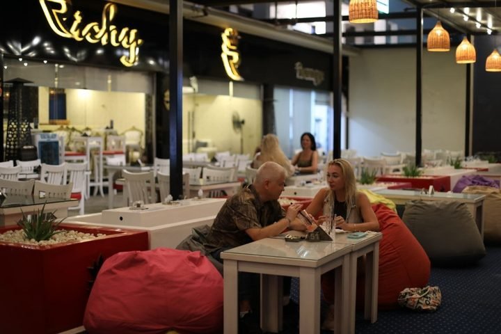 Two guests at a terrace table under the lit Richy sign